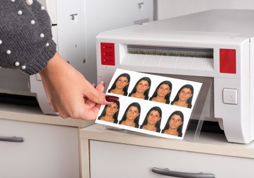 Set of just printed passport photos of a young woman exiting the printer with the hand of a woman reaching for the sheet in a close up view